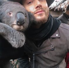 a man holding a koala in his arms and wearing a hat on top of him