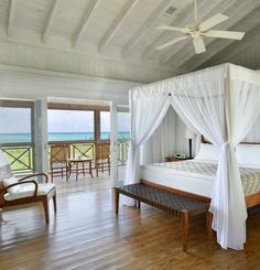 a bedroom with a white canopy bed sitting on top of a hard wood floor next to an ocean view