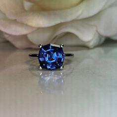 a blue ring sitting on top of a table next to a white rose with petals in the background