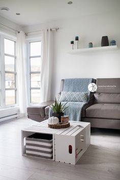 a living room filled with furniture next to large windows and white walls on either side of the couch