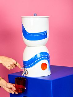 a woman is holding a cup in front of a large vase on top of a blue table