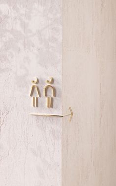 two small wooden figures on a white and beige wall next to a hook with an arrow