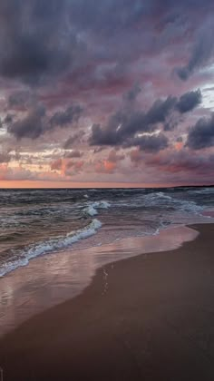 an ocean beach with waves coming in to the shore and dark clouds above it at sunset