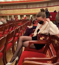 a woman sitting on a red chair in a room with rows of chairs and people standing around