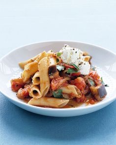 a white bowl filled with pasta and sauce on top of a blue tablecloth next to a fork