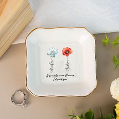 a white and gold plate with two flowers on it next to a pair of wedding rings