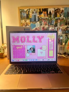 an open laptop computer sitting on top of a wooden desk next to a pile of pictures