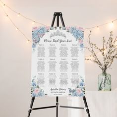 a blue and white wedding seating chart on a easel with lights in the background