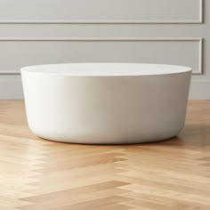 a large white bowl sitting on top of a wooden floor in front of a wall