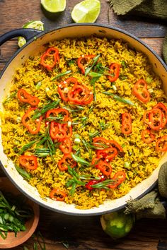 a large pot filled with rice and vegetables on top of a wooden table next to limes