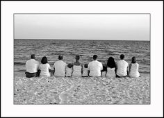 four people sitting on the beach looking out at the water