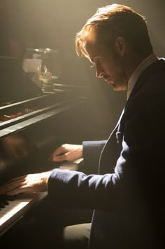 a man sitting at a piano with his hands on the keyboard and light coming from behind him