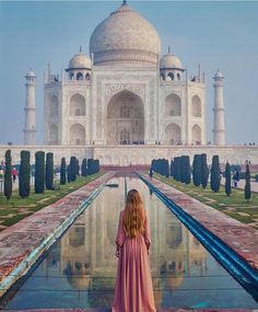 a woman standing in front of the tajwa mosque, with her reflection in the water