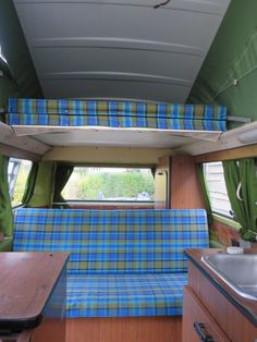 the interior of a camper with green curtains and blue plaid fabric on the couch