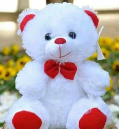 a white teddy bear with a red bow tie sitting in front of some yellow flowers