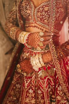 a woman in a red and gold bridal outfit with her hands on her hips