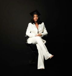 a woman sitting on top of a chair wearing a white suit and black graduation hat