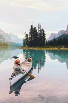 a person in a canoe paddling on the water with mountains and pine trees in the background