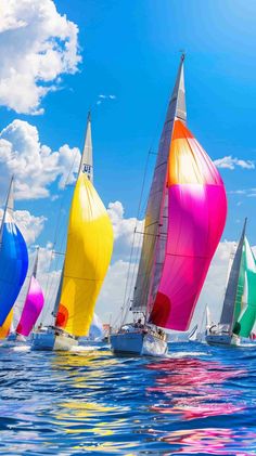 colorful sailboats sailing in the ocean on a sunny day with blue sky and clouds