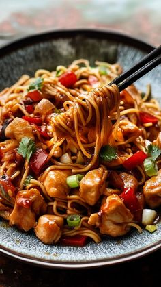 a plate of noodles with chicken and vegetables being held by chopsticks over it