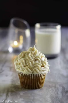 a cupcake with white frosting sitting on a table next to a glass of milk