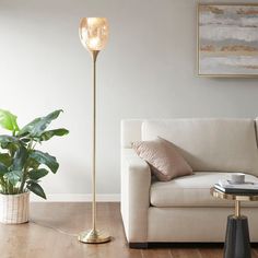 a living room with a white couch and a gold floor lamp in the corner next to a potted plant