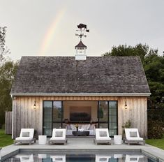 a pool house with a rainbow in the background and lawn chairs by the swimming pool