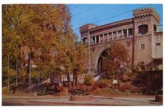 an old building with trees and bushes in the foreground, on a sunny day