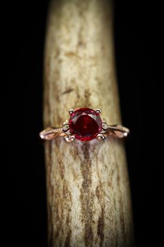 a close up view of a ring with a red stone in the center on a piece of wood