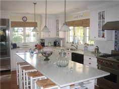 a large kitchen with white cabinets and marble counter tops, stainless steel appliances and an island in the middle