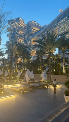 an outdoor area with palm trees and white umbrellas in front of tall buildings at dusk