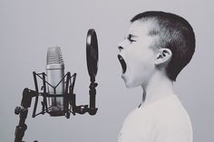 a young boy singing into a microphone in front of a gray background with black and white images