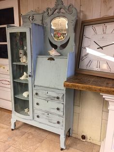 an old blue cabinet with a mirror on top and drawers below it, in front of a wall clock