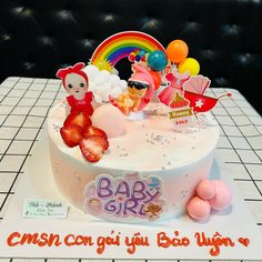 a birthday cake decorated with dolls and balloons on a table top, in the shape of a baby girl