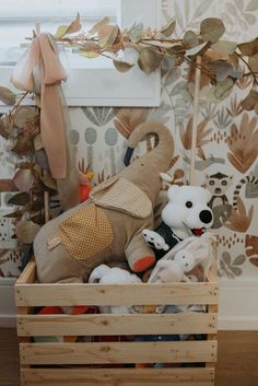 A detailed shot of stuffed animals in a wooden crate in a baby boy's nursery. There is fun printed wallpaper lining the walls.