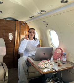 a woman is sitting in an airplane with her laptop on the table and holding a drink