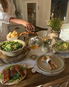 a woman pours wine into a bowl filled with salad and other foods on a table