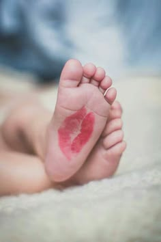 a baby's foot with a red lip stain on the top of its toe