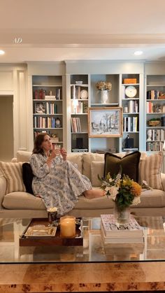 a woman sitting on a couch in front of a book shelf filled with lots of books