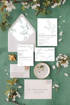 the wedding stationery is laid out on a green surface with white flowers and greenery