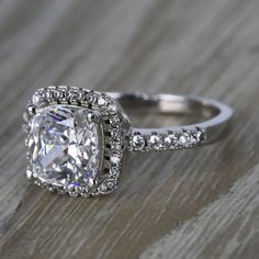 an engagement ring with a cushion cut diamond surrounded by pave diamonds on a wooden surface