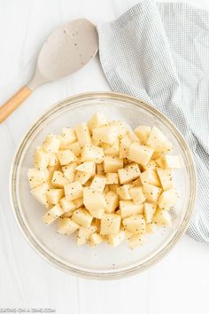 a glass bowl filled with diced potatoes next to a wooden spoon and cloth on a white surface