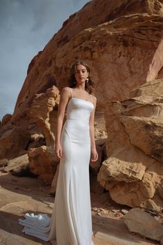 a woman standing in front of rocks wearing a white dress