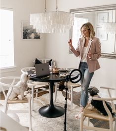 a woman standing in front of a laptop computer on top of a table next to a dog