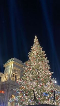 a large christmas tree is lit up in front of a white building with lights on it