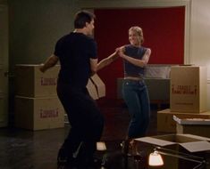 a man and woman are dancing in an empty room with boxes on the floor behind them