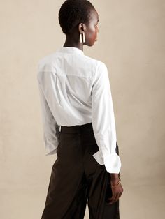 A seamless silhouette, this soft tuxedo shirt is made from 100% cotton with a concealed button front, elegant pintuck detail and exaggerated cuffs.  SEMI-FITTED: Cut for a not-too-tight, not-too-loose fit.  Banded collar.  Hidden button front.  Troca Tailored Tops With Fold Down Collar For Work, Timeless Tailored Tops For Office, Timeless Fitted Tops For Workwear, Timeless Fitted Tops For Work, Classic Tailored Office Top, Classic Tailored Office Tops, Classic Tailored Tops For Office, Tailored Top With Concealed Placket For Workwear, Modern Workwear Tops With Concealed Placket