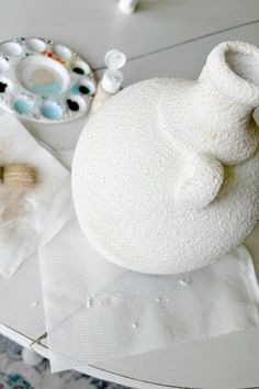 a white vase sitting on top of a table next to some other items and paint