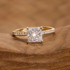 a princess cut diamond ring on top of a wooden surface