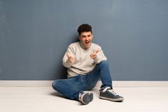 a young man sitting on the floor with his thumbs up and looking at the camera